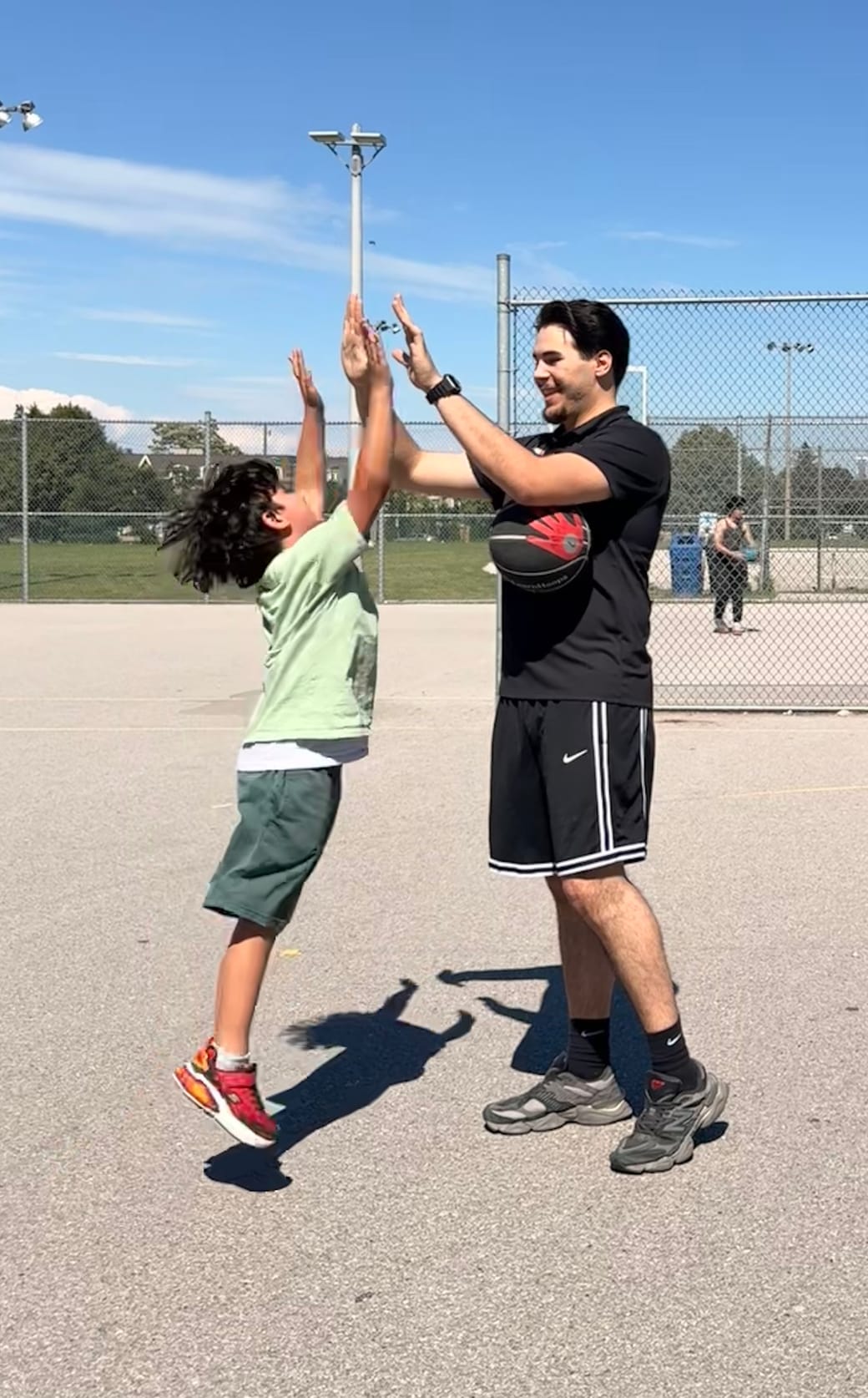 URAZ HOOPS coach sharing a high-five with a young player after a drill on an outdoor court