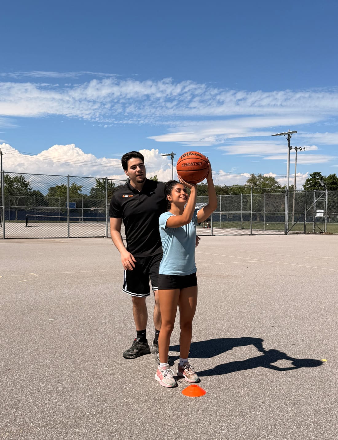 URAZ HOOPS coach guiding a young player's shooting form on an outdoor court in Vaughan