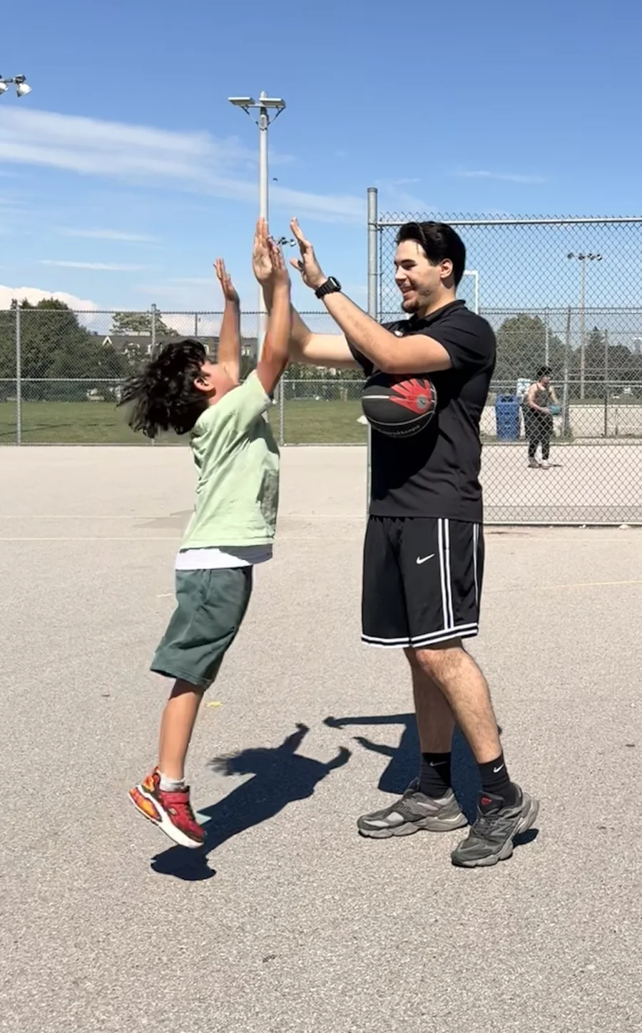 Mert Uraz sharing a high-five with a young player after an outdoor drill